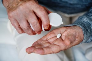 Older person shaking a sinlge pill out of an open medicine bottle